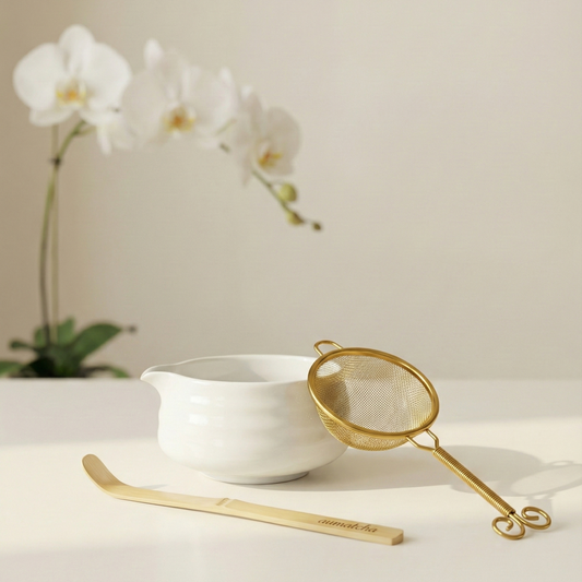 White bowl with gold spoon and strainer on a light surface with white orchids in the background