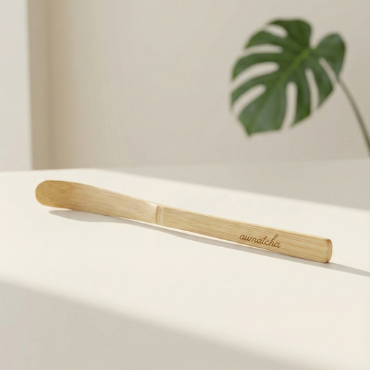 Bamboo tea spoon with 'aumatcha' branding on a light surface with a plant in the background
