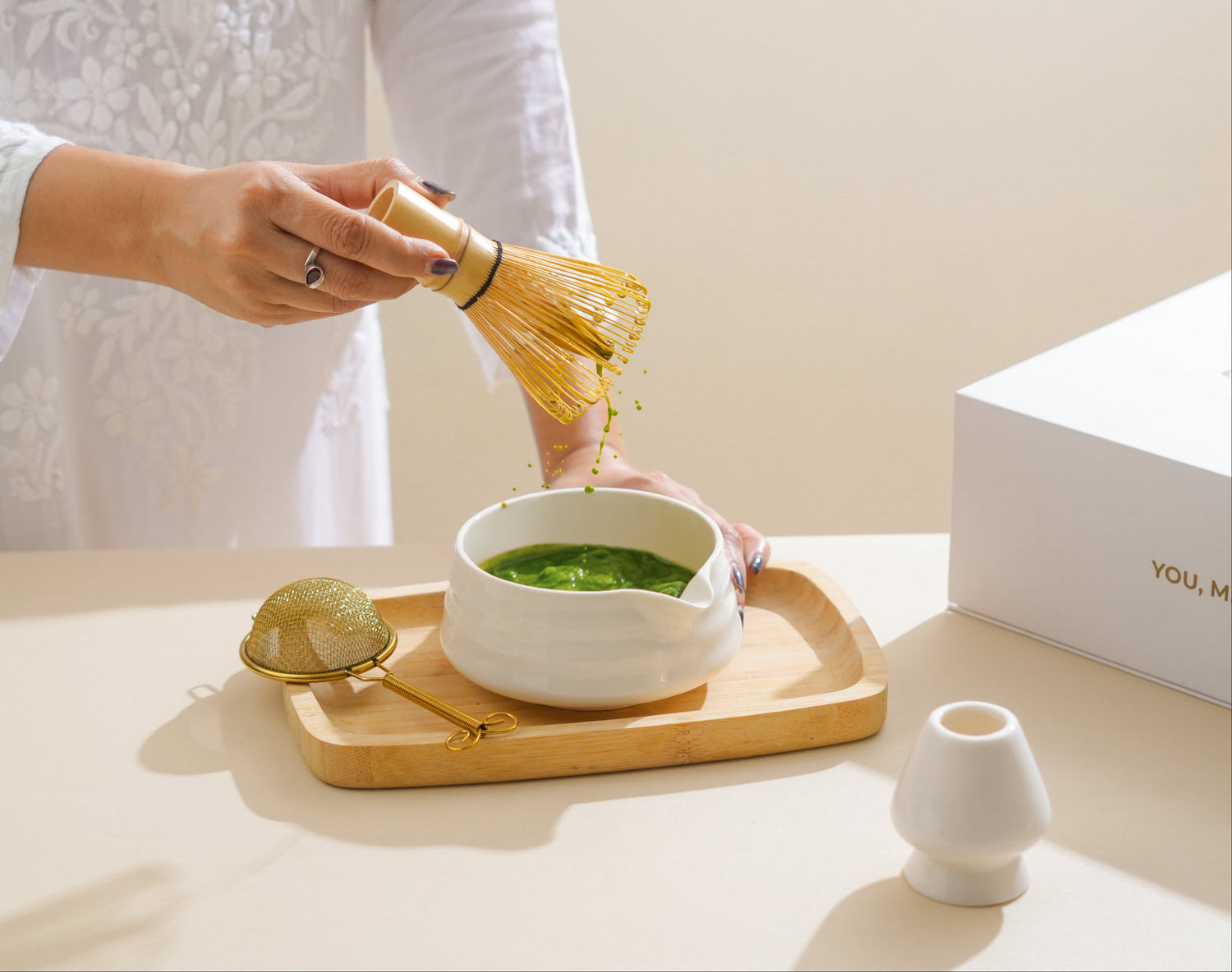 Person pouring green tea into a white cup on a wooden tray with a plain background