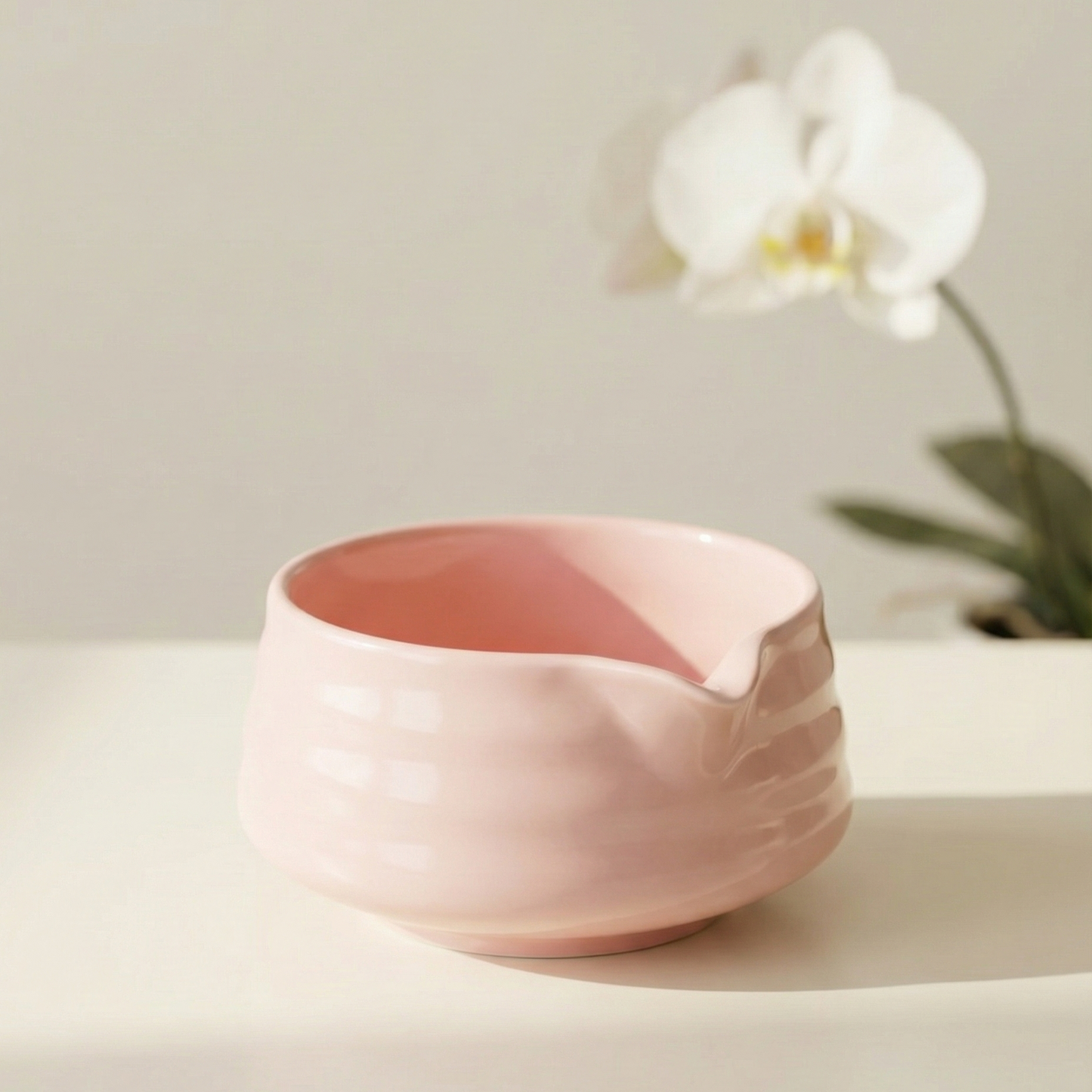 Pink ceramic bowl on a light surface with a blurred white flower in the background